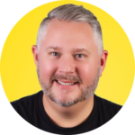 Sam Demma Smiling person with short, gray hair and beard against a bright yellow background, wearing a black shirt—Sam Demma from Elite Speaker Coaching. Elite Speaker Coaching